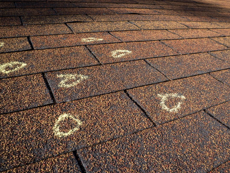 Hail strikes circled in chalk on weathered asphalt shingles