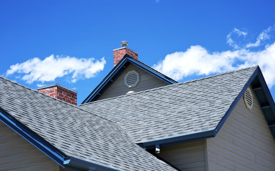 Grey architectural shingles along a roofline, with a brick chimney